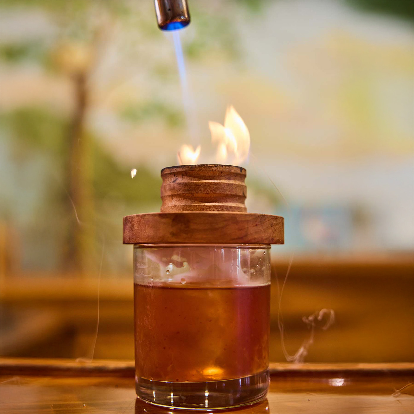 Old fashioned cocktail being smoked with fire torch.