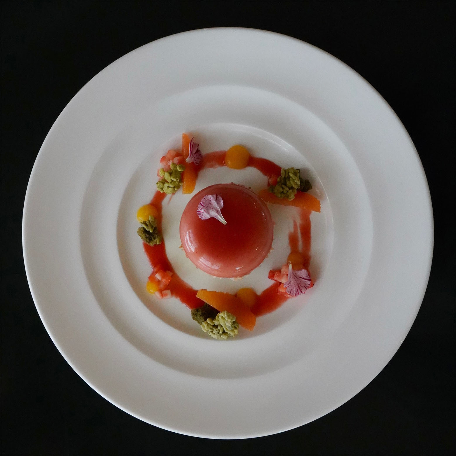 Looking straight down on a gelatin appetizer in a ring of tiny bites and orange drizzle
