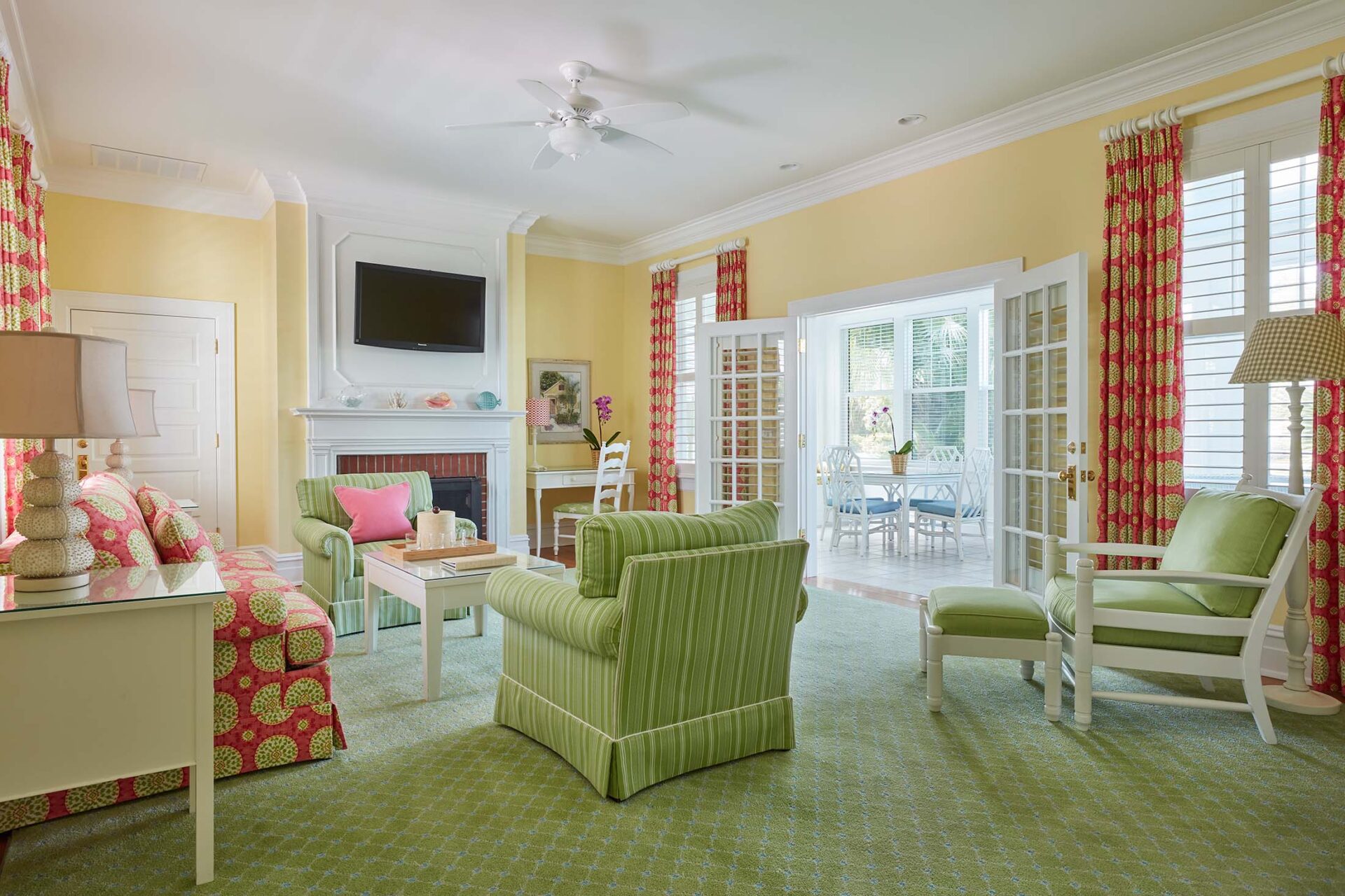 Looking from a lush living room with a variety of colorful furniture and red-patterned curtains out onto a sunroom