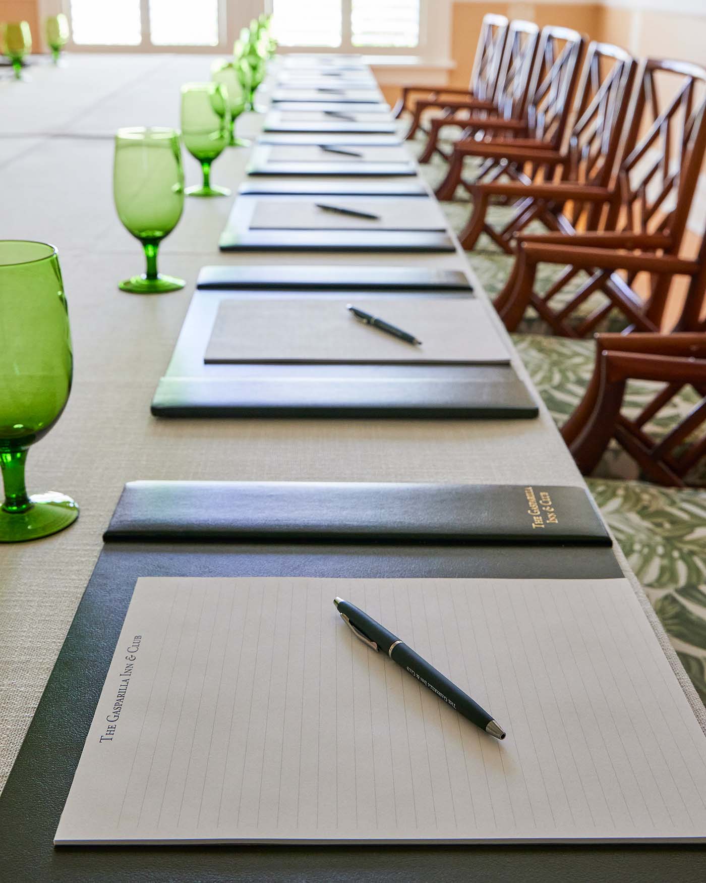 Close-up of a series of notepads and pens and green water glasses on a conference table