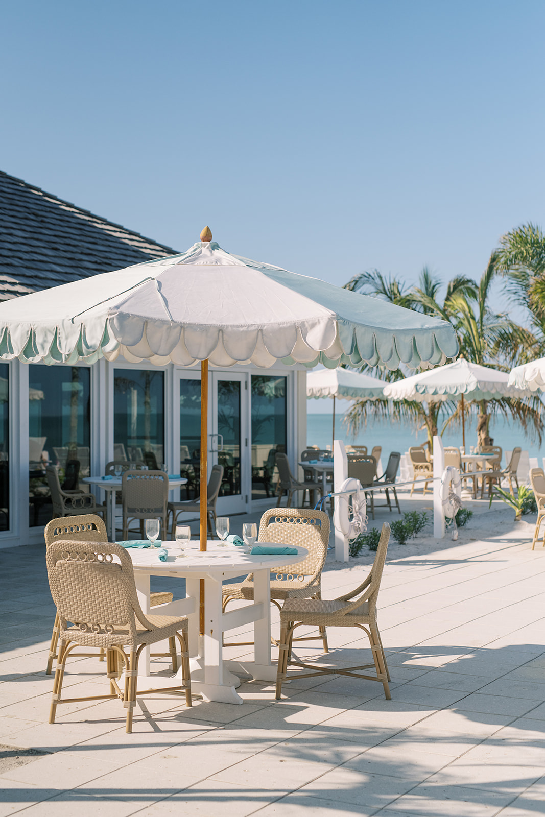 Wicker four-top dinette set shaded by a white patio umbrella in a lovely oceanfront setting