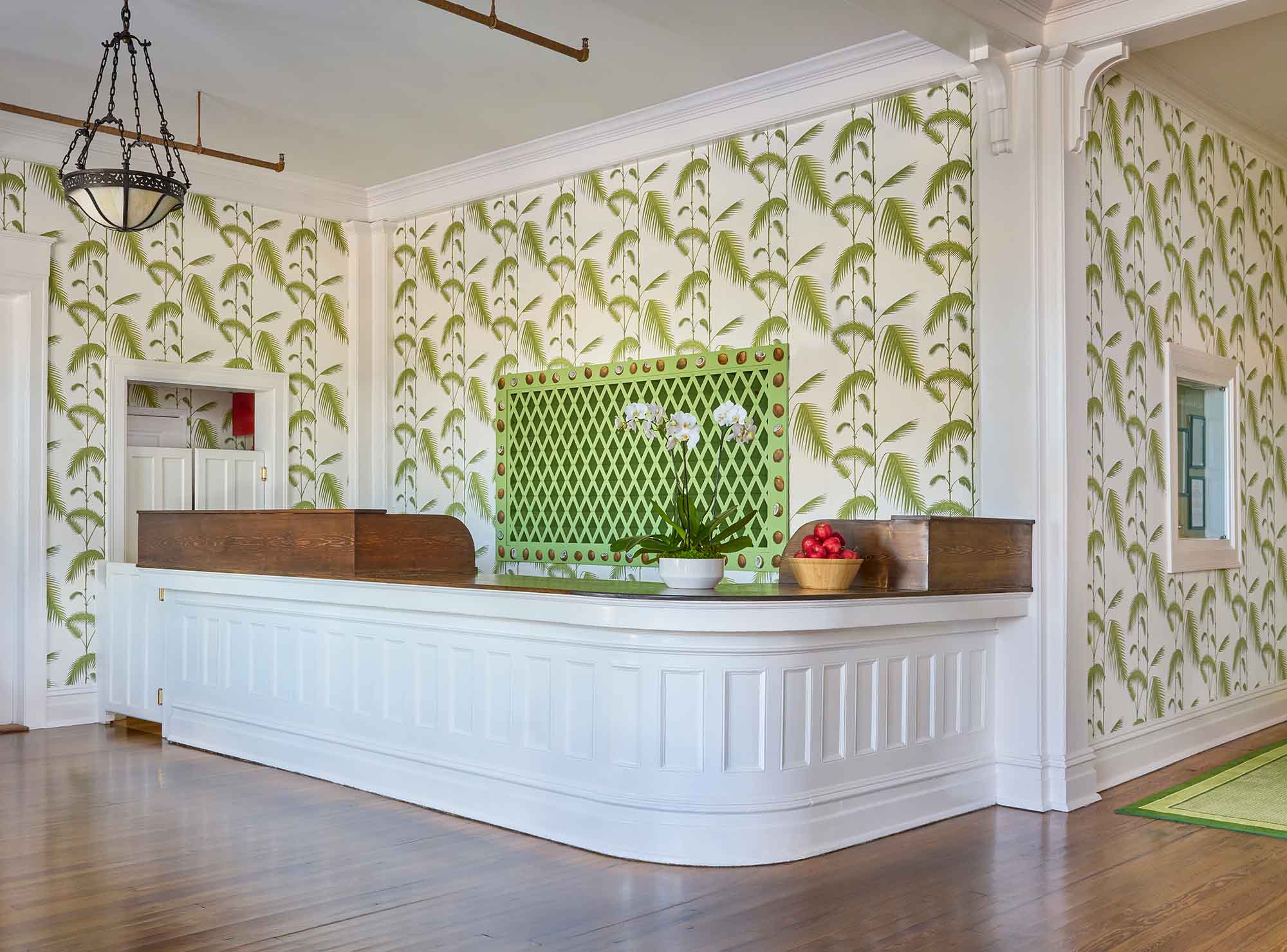 A large, curved front desk decorated with a basket of ripe red apples and a small plant in a white bowl