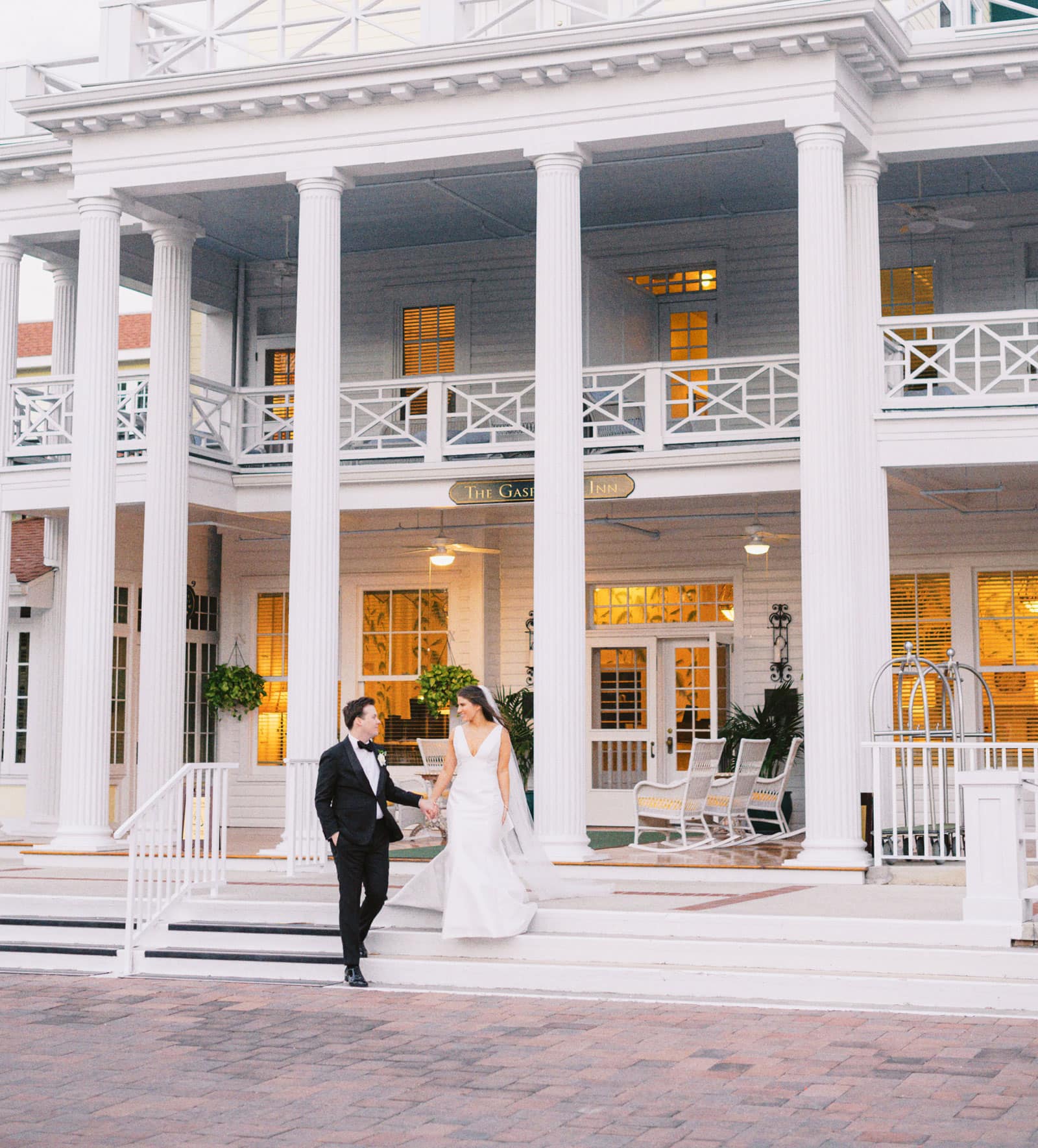 The Inn's white colonnade and entablature serve as backdrop to a tuxedoed groom guiding his bride down the veranda stairs