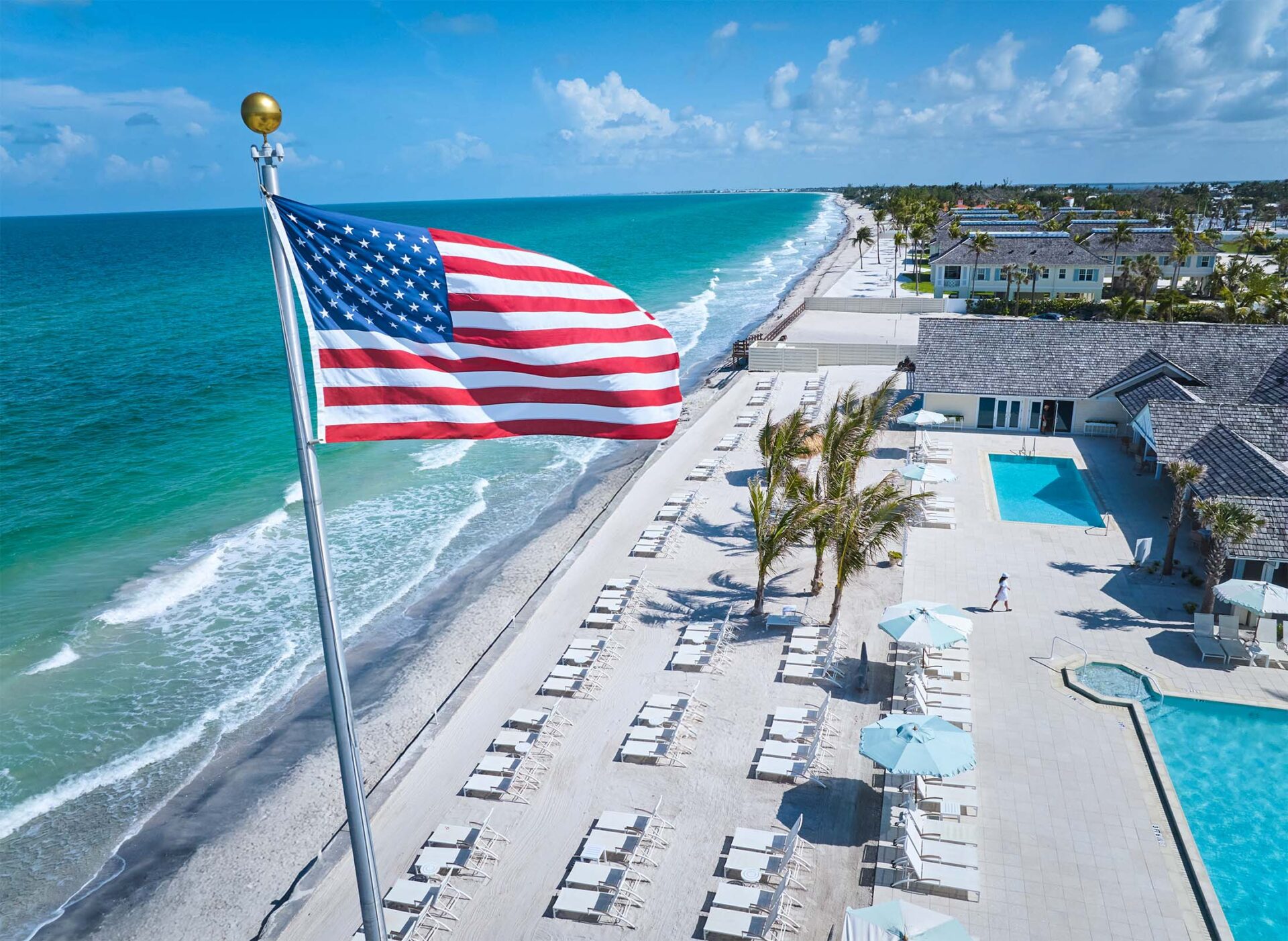 American flag waves above ocean and beach club with pools.