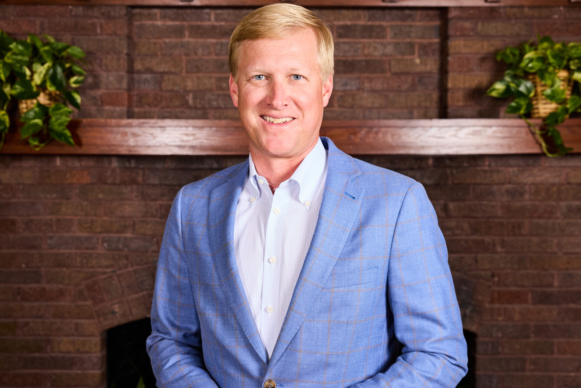 Portrait of man smiling looking at camera wearing a blue blazer in front of a mantle
