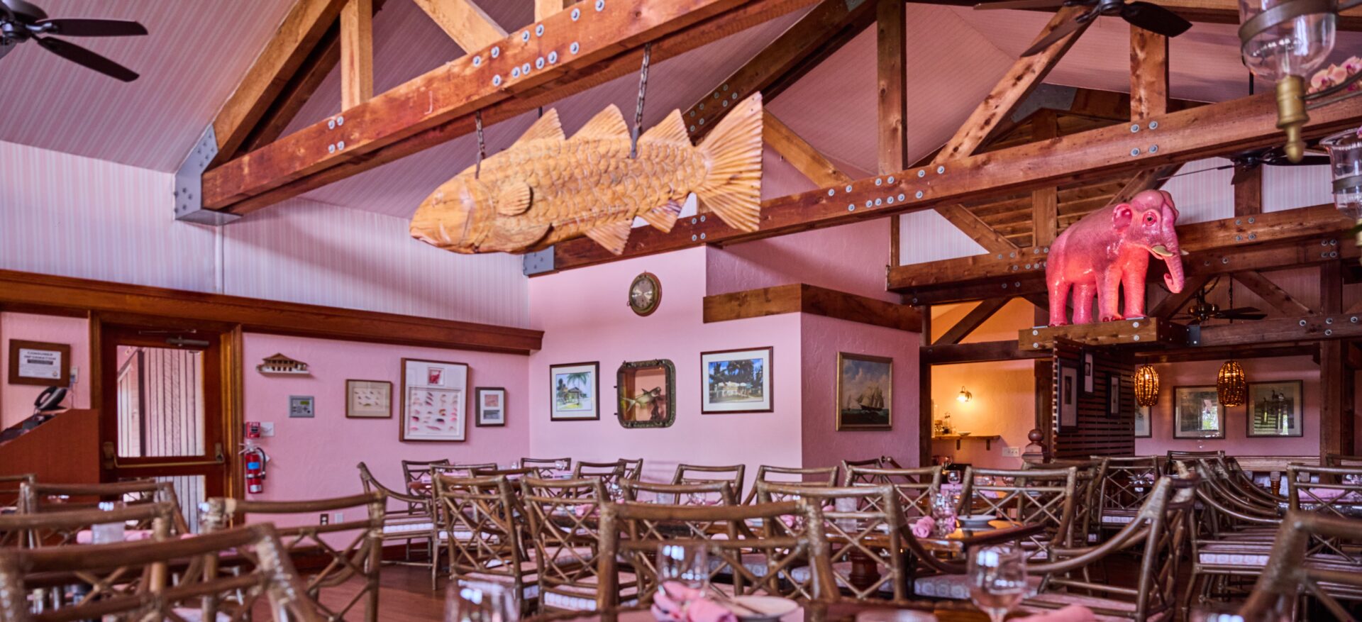 Restaurant with wooden chairs, pink walls and a big pink elephant statue.