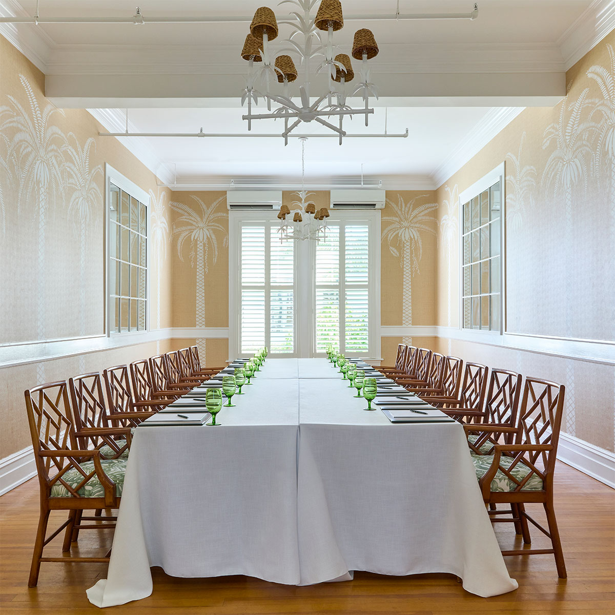 Long table with white table cloth with green glasses and notebooks at each chair