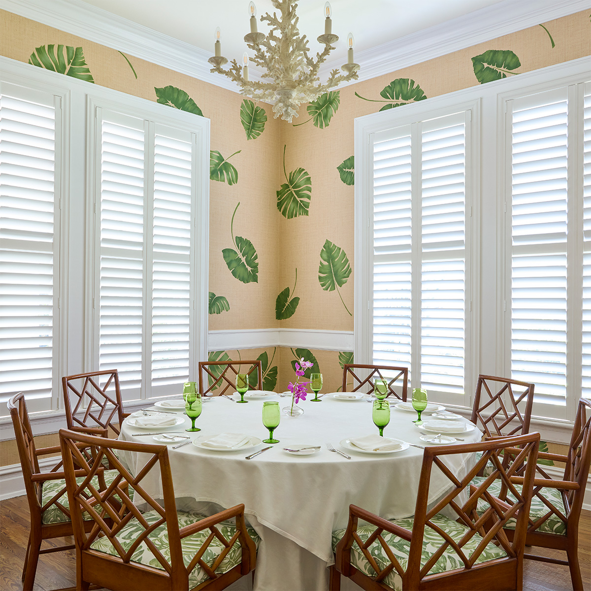 Round table with place settings in intimate room in front of windows botanical leaf pattern on walls.