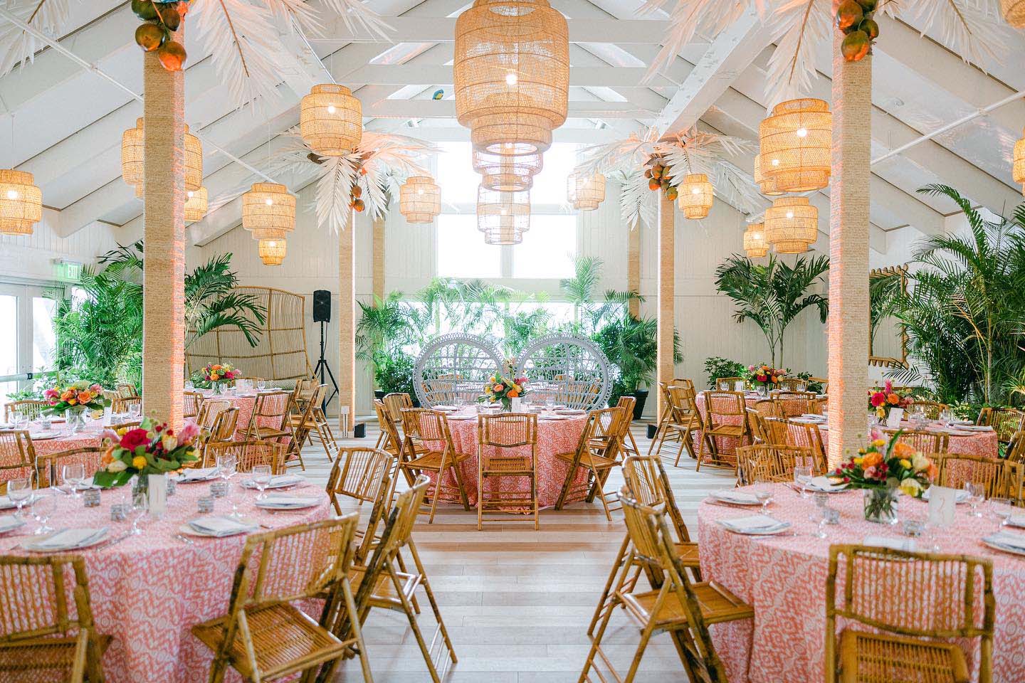 Sun filled large space set for a casual reception tables with pink table and wicker chairs.